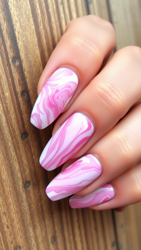 Close-up of manicured nails with a pink and white marble effect on a wooden surface.