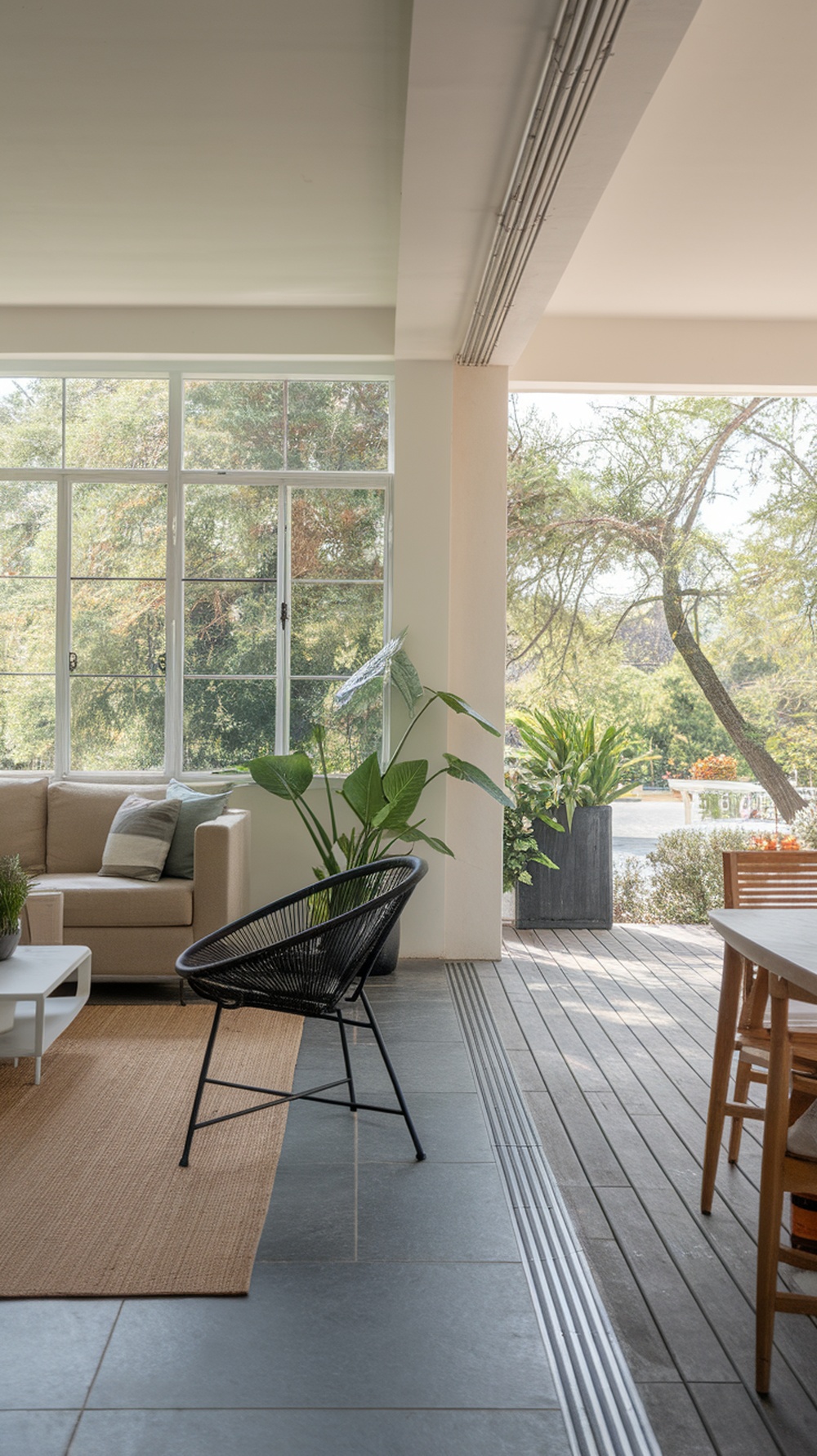 A bright living room with large windows, a cozy sofa, potted plants, and an outdoor deck visible.