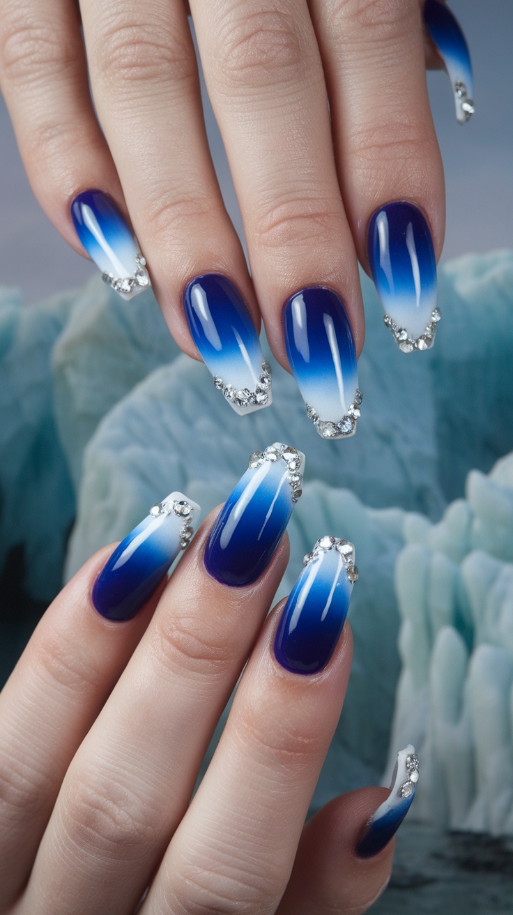 A set of glacier blue ombre acrylic nails with rhinestones, showcasing a gradient from deep blue to icy white.