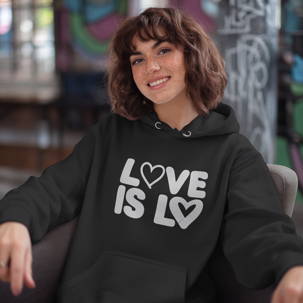 A person wearing a black hoodie with 'Love Is Love' printed on the front, smiling in a vibrant setting.