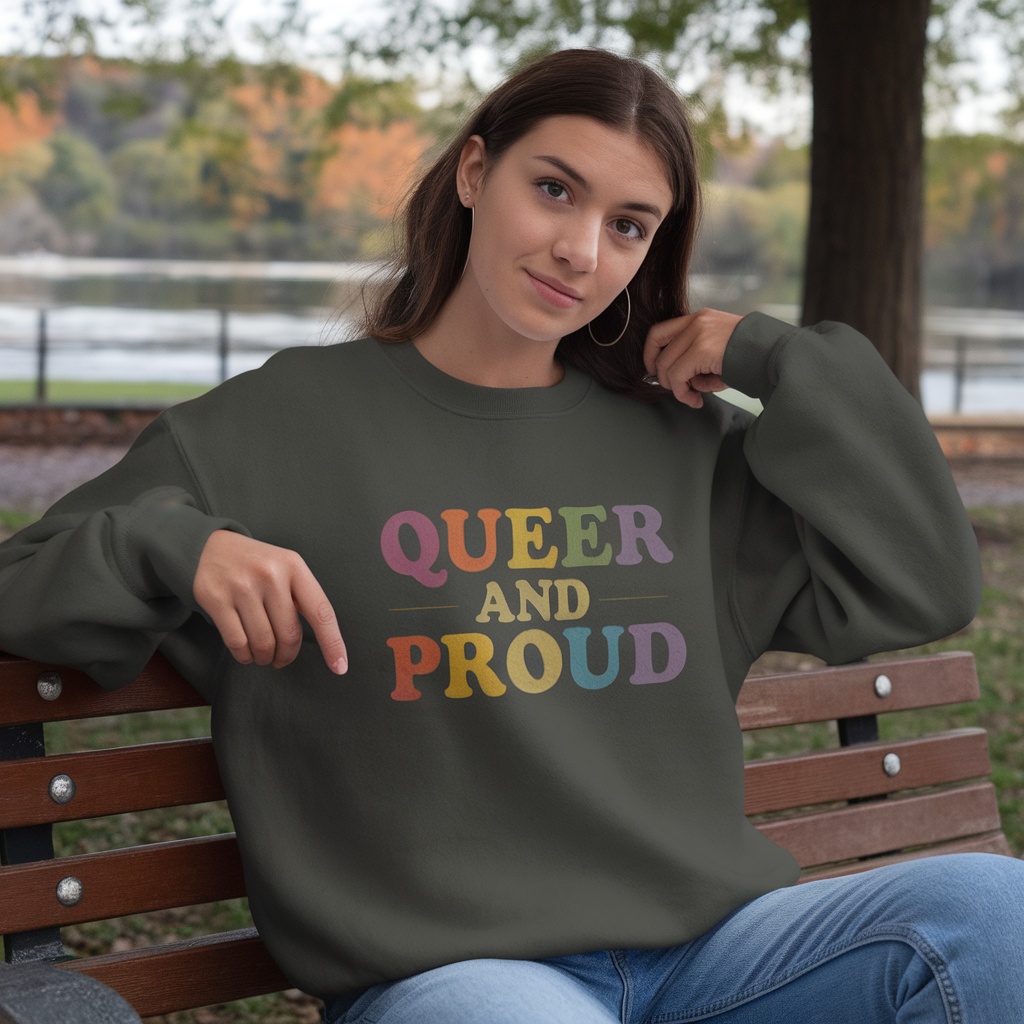A person wearing a 'Queer and Proud' sweatshirt sitting on a bench.