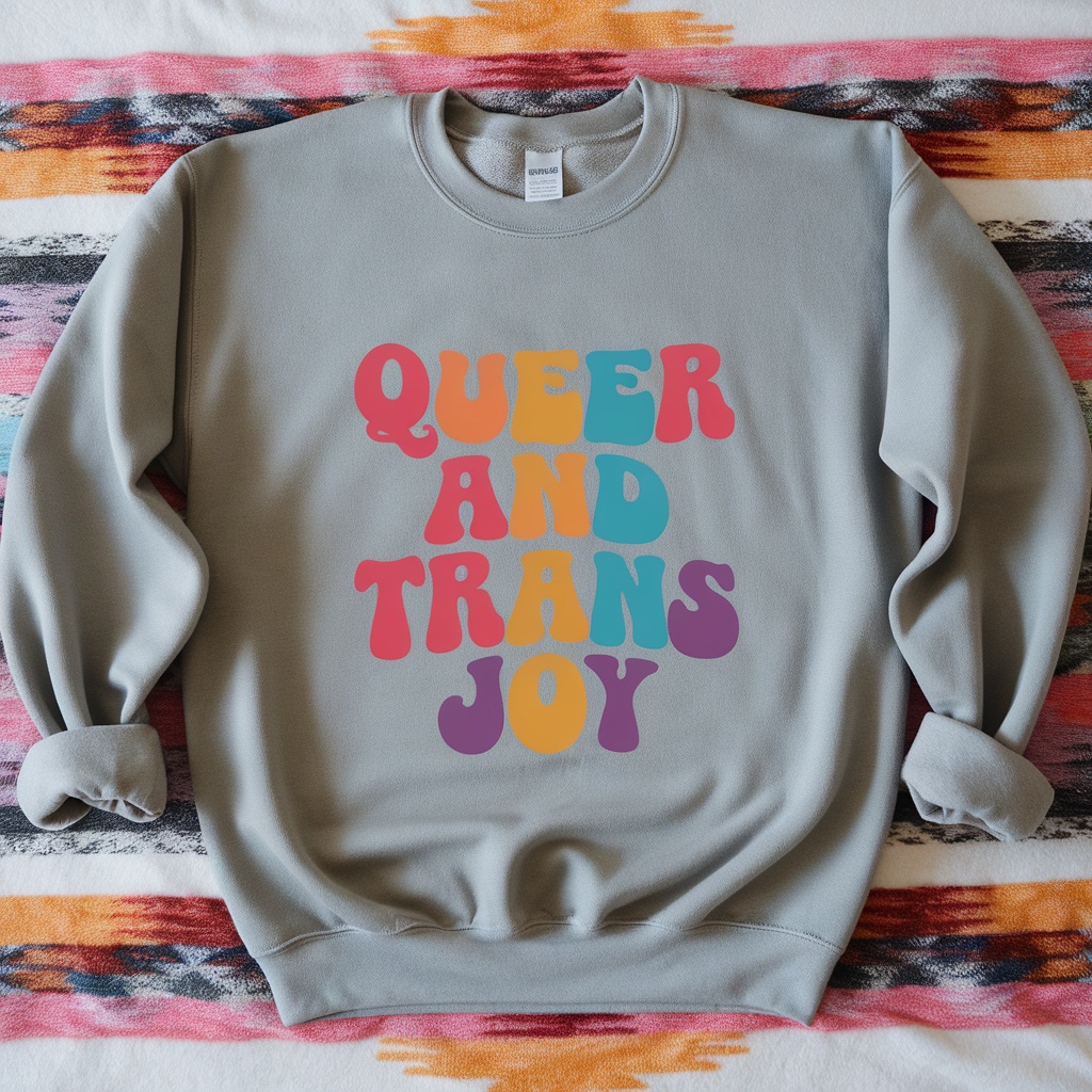 A cozy gray sweatshirt with the text 'Queer And Trans Joy' in colorful letters.