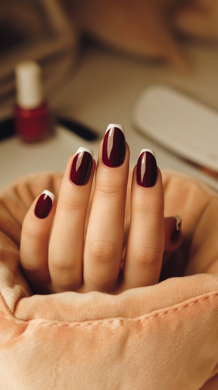 Close-up of hands with dark cherry red nails featuring white tips, resting on a soft fabric.