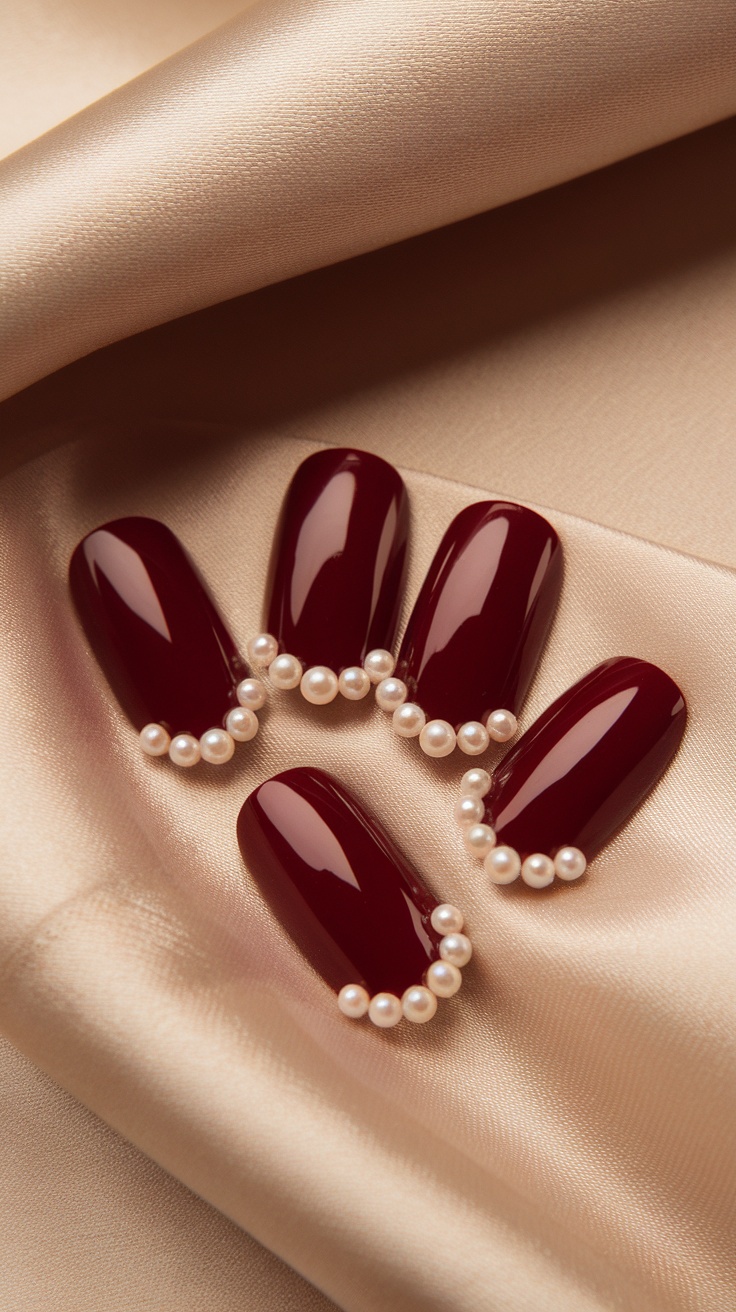 Dark cherry red nails with pearl accents on a satin background