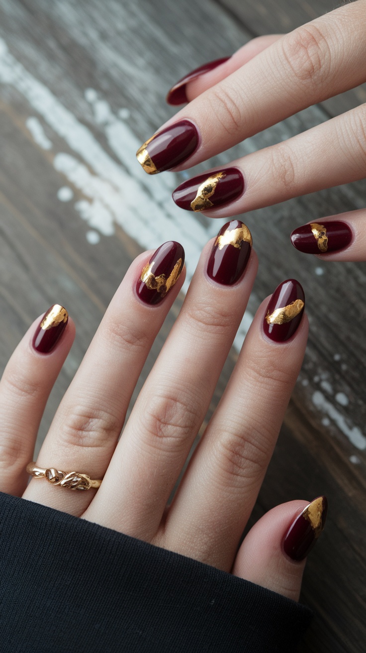 Dark cherry red nails with gold foil accents on a wooden surface