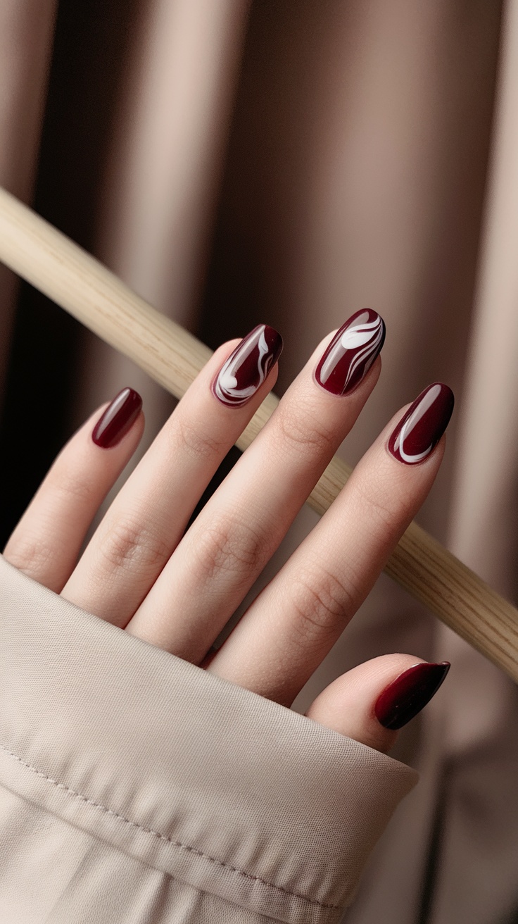 A hand with dark cherry red marble effect nails featuring white swirls.