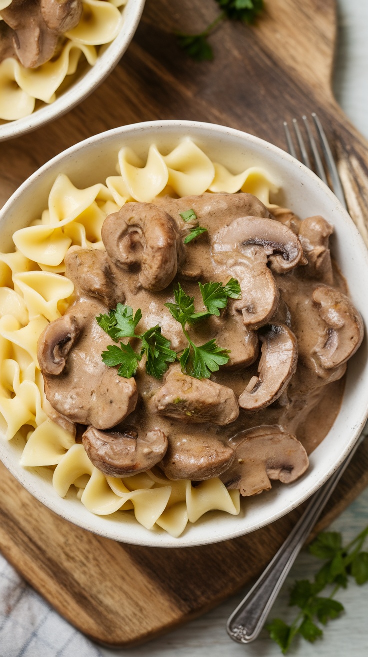 A bowl of beef stroganoff served over egg noodles with mushrooms and parsley garnish.