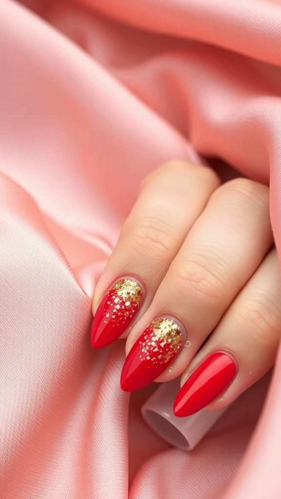 A hand with crimson red nails featuring a gold glitter gradient, resting on a pink satin background.