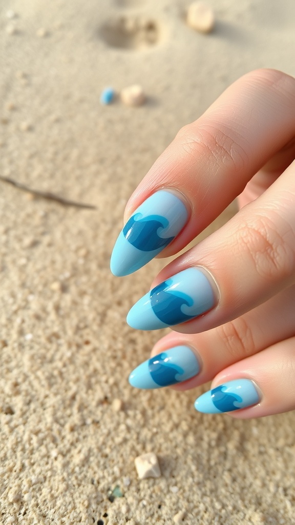 Close-up of ocean-inspired blue almond-shaped nails with wave designs on a sandy background.