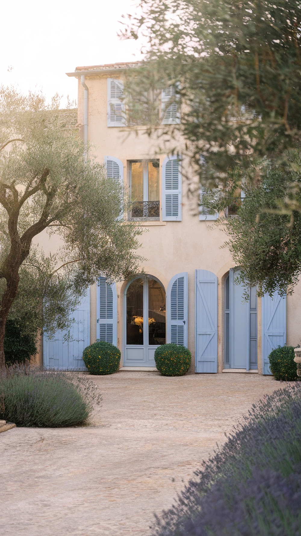 A French country house with blue shutters and a cobblestone driveway, surrounded by greenery and lavender.