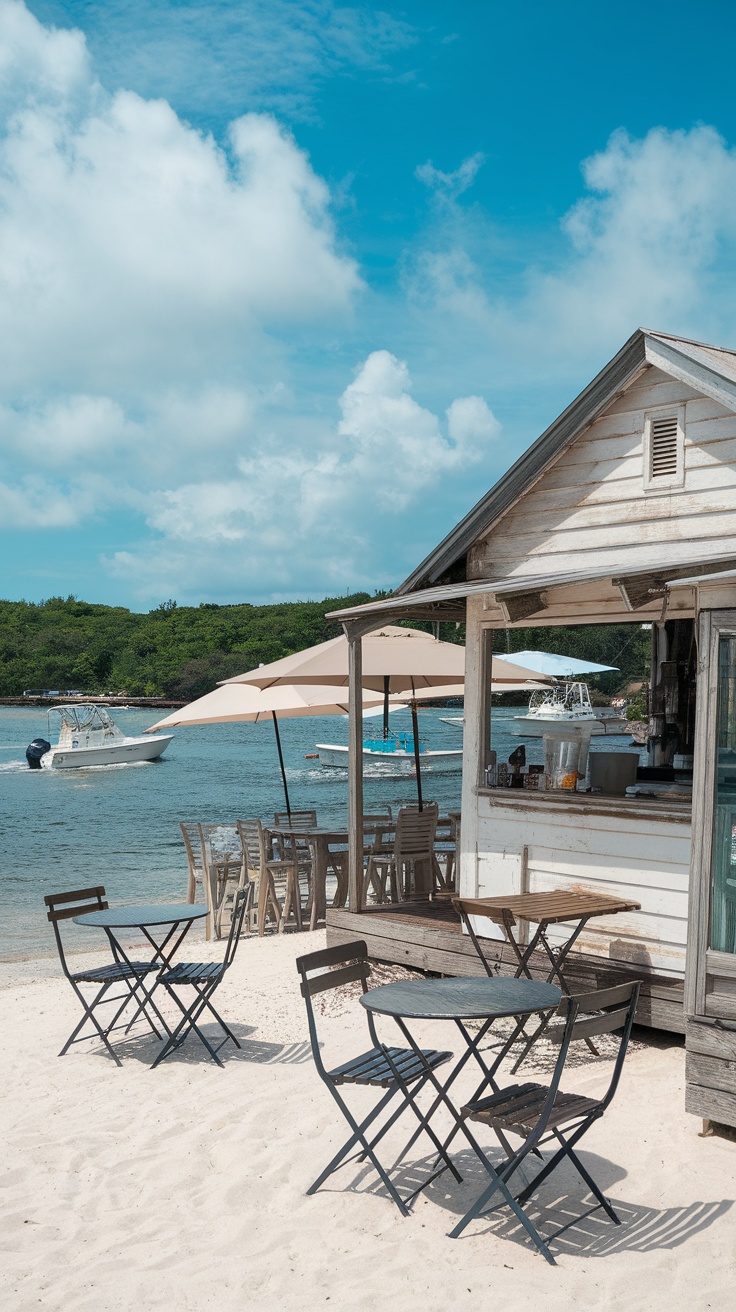 A beachside seafood shack with tables on the sand and boats in the water.