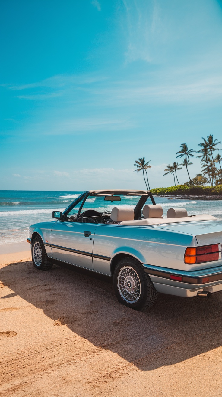 A BMW E30 325I Convertible parked on a sandy beach with palm trees and ocean in the background.