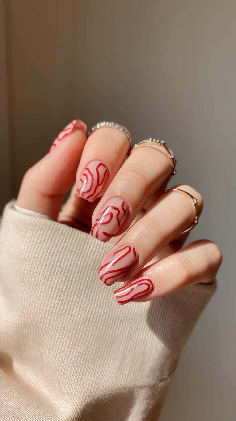 A close-up of abstract red nail art featuring red swirls on a nude base.