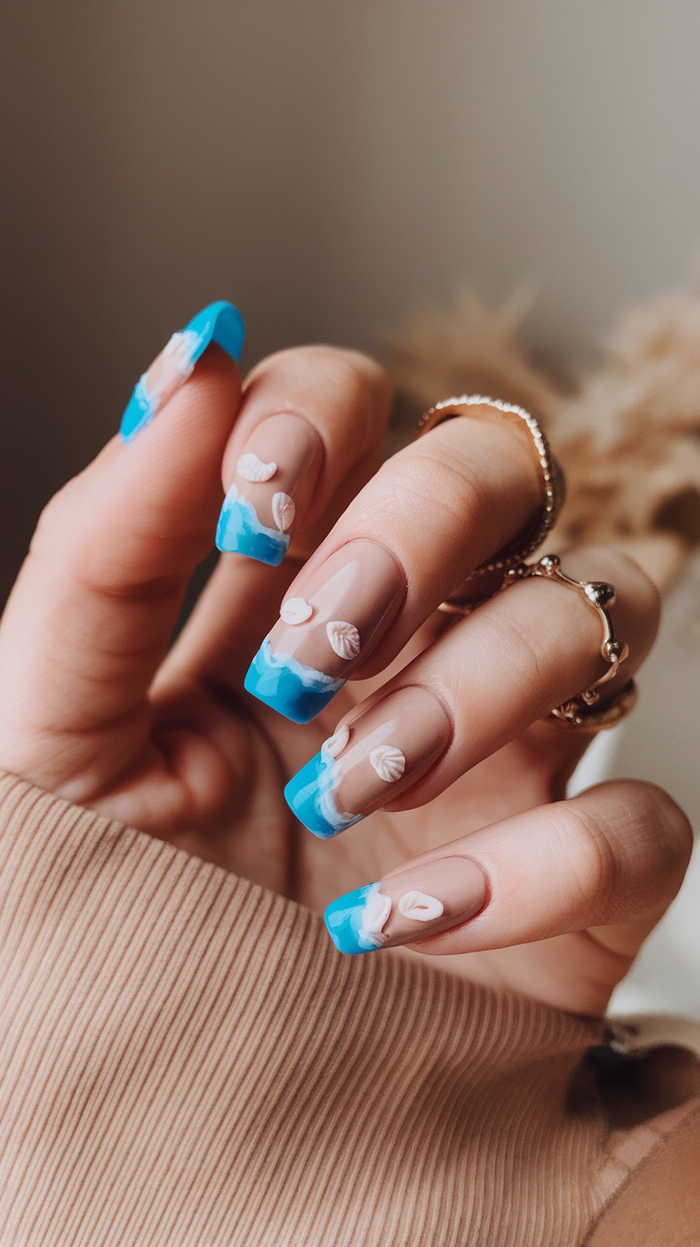 Nail design featuring beachy colors with blue tips and white shell accents.
