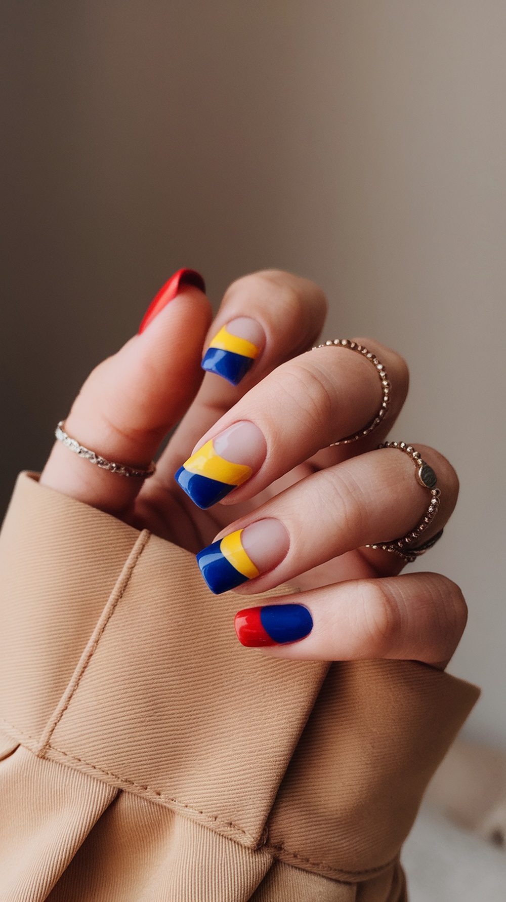 A hand with short nails featuring bold color blocking in red, blue, and yellow.