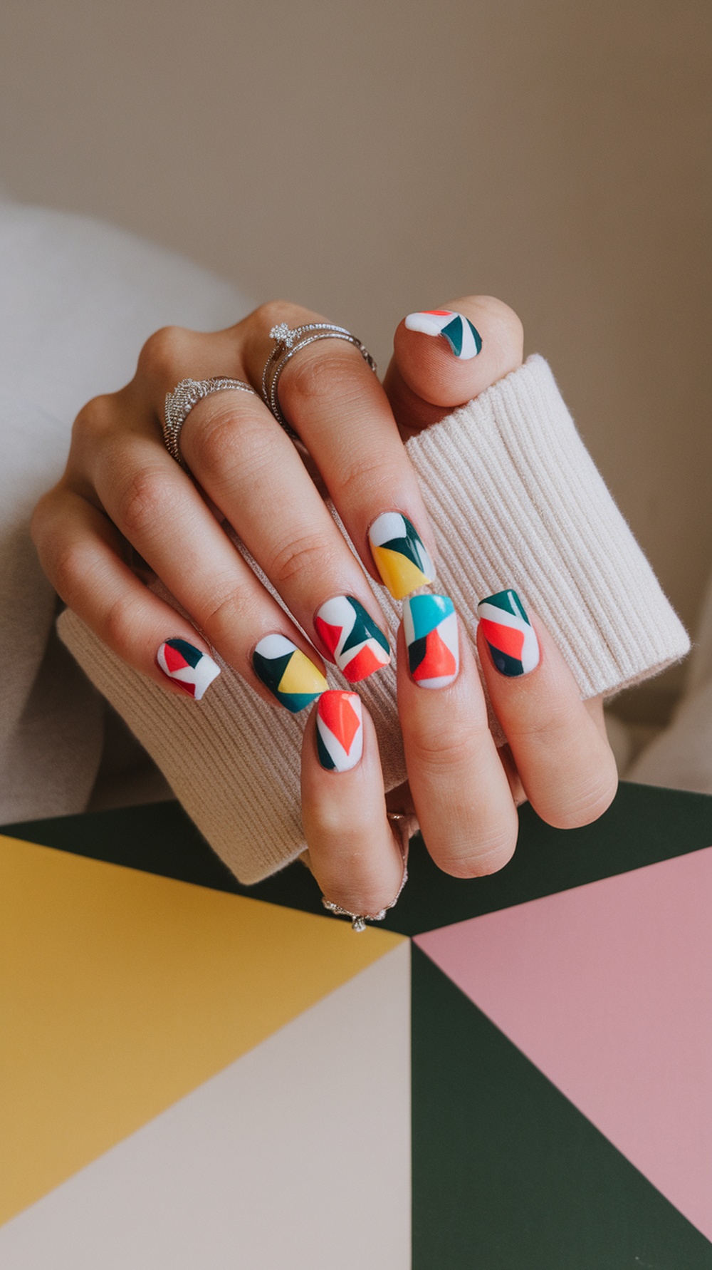 A close-up of hands with colorful geometric nail designs, featuring red, green, yellow, and blue patterns.