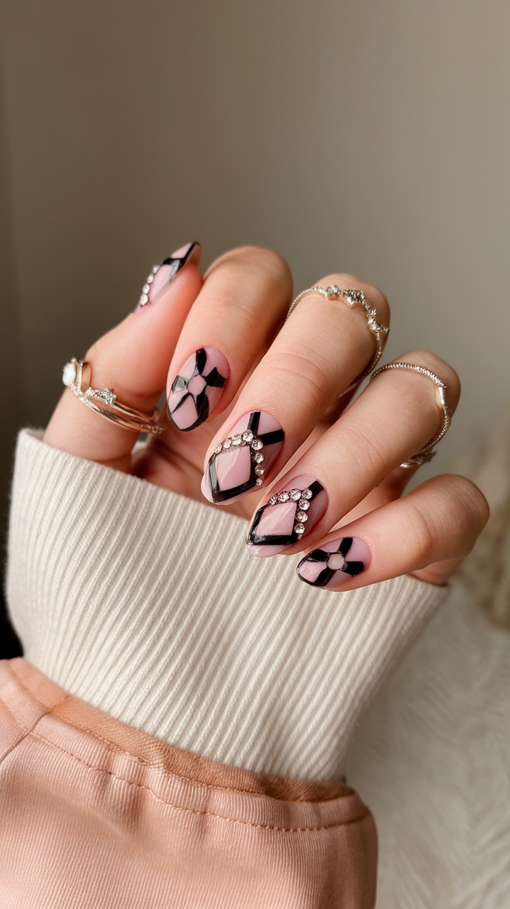 Nails with bold geometric patterns in pink and black, adorned with rhinestones.