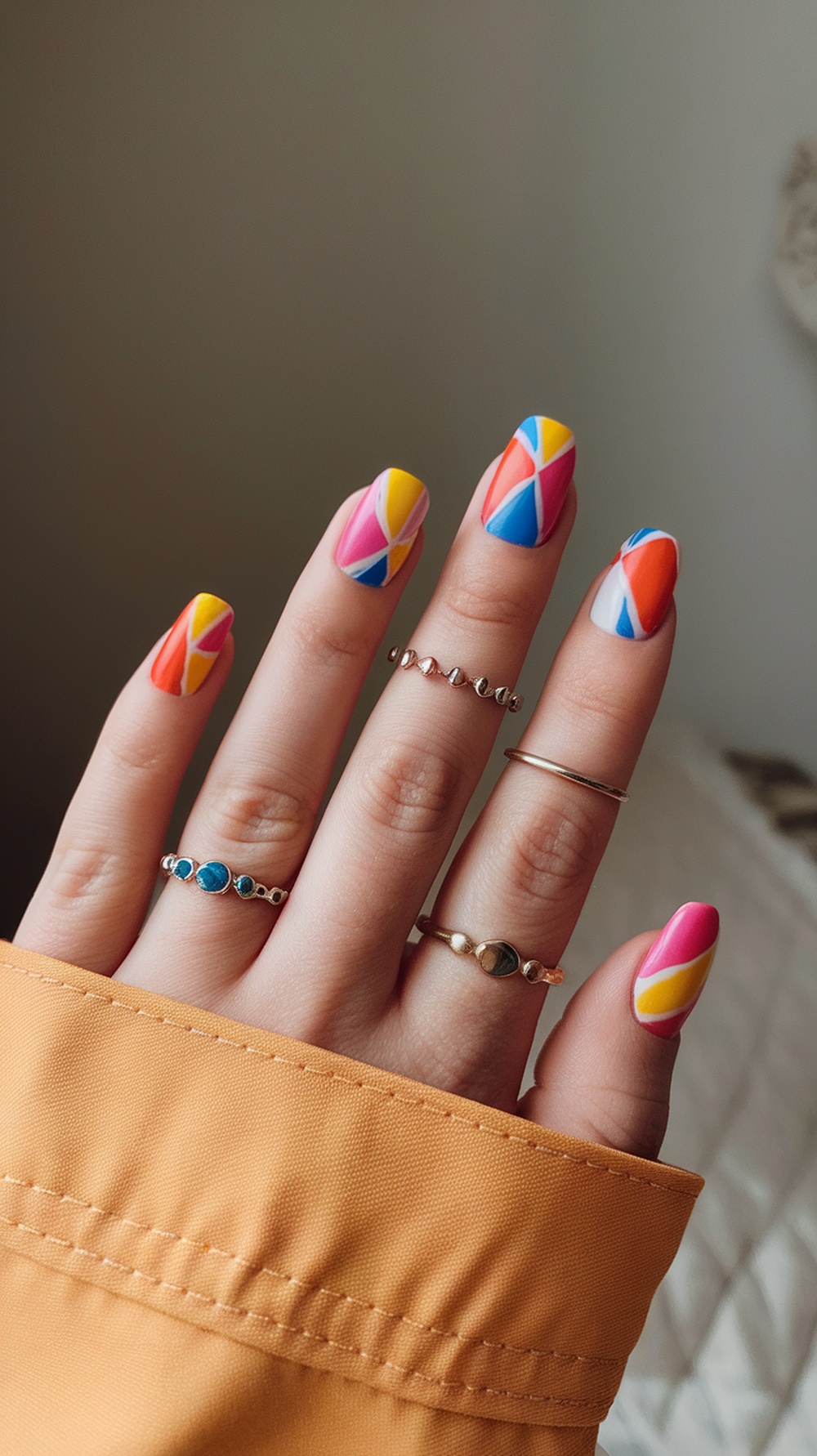 A hand with colorful geometric nail art featuring bright patterns and rings.