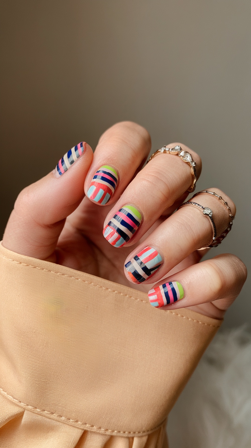 A close-up of short nails featuring bold stripes and dots in vibrant colors.