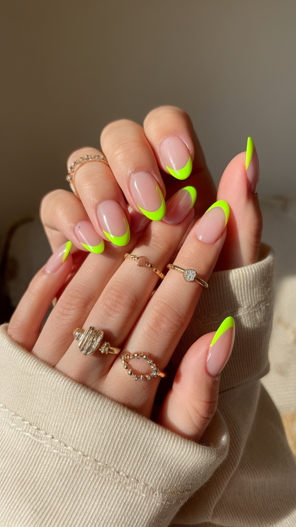 Close-up of hands with bright neon green almond-shaped nails and delicate gold rings