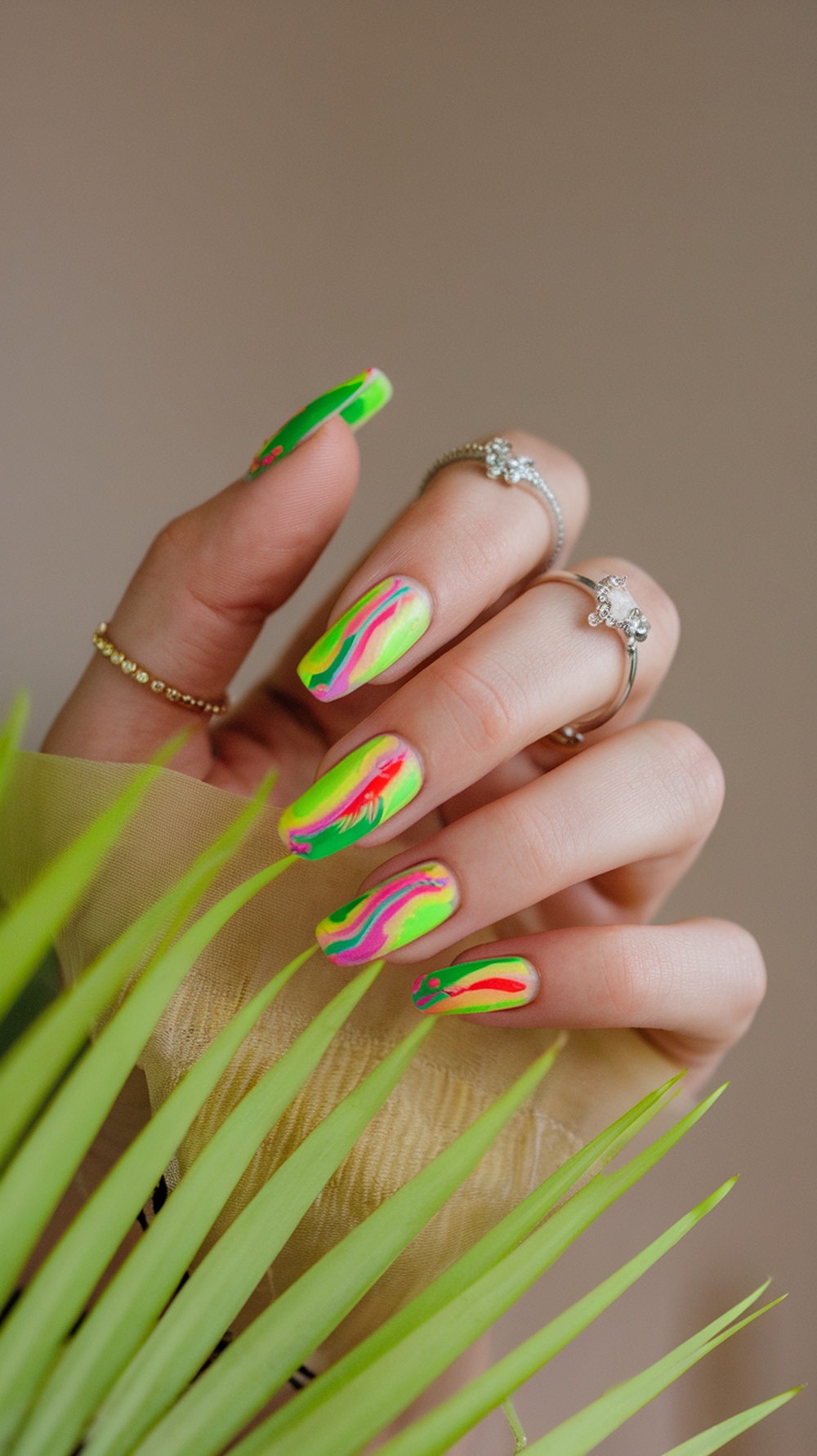 A hand with bright neon colored nails featuring green, pink, and yellow swirls, holding a green plant.