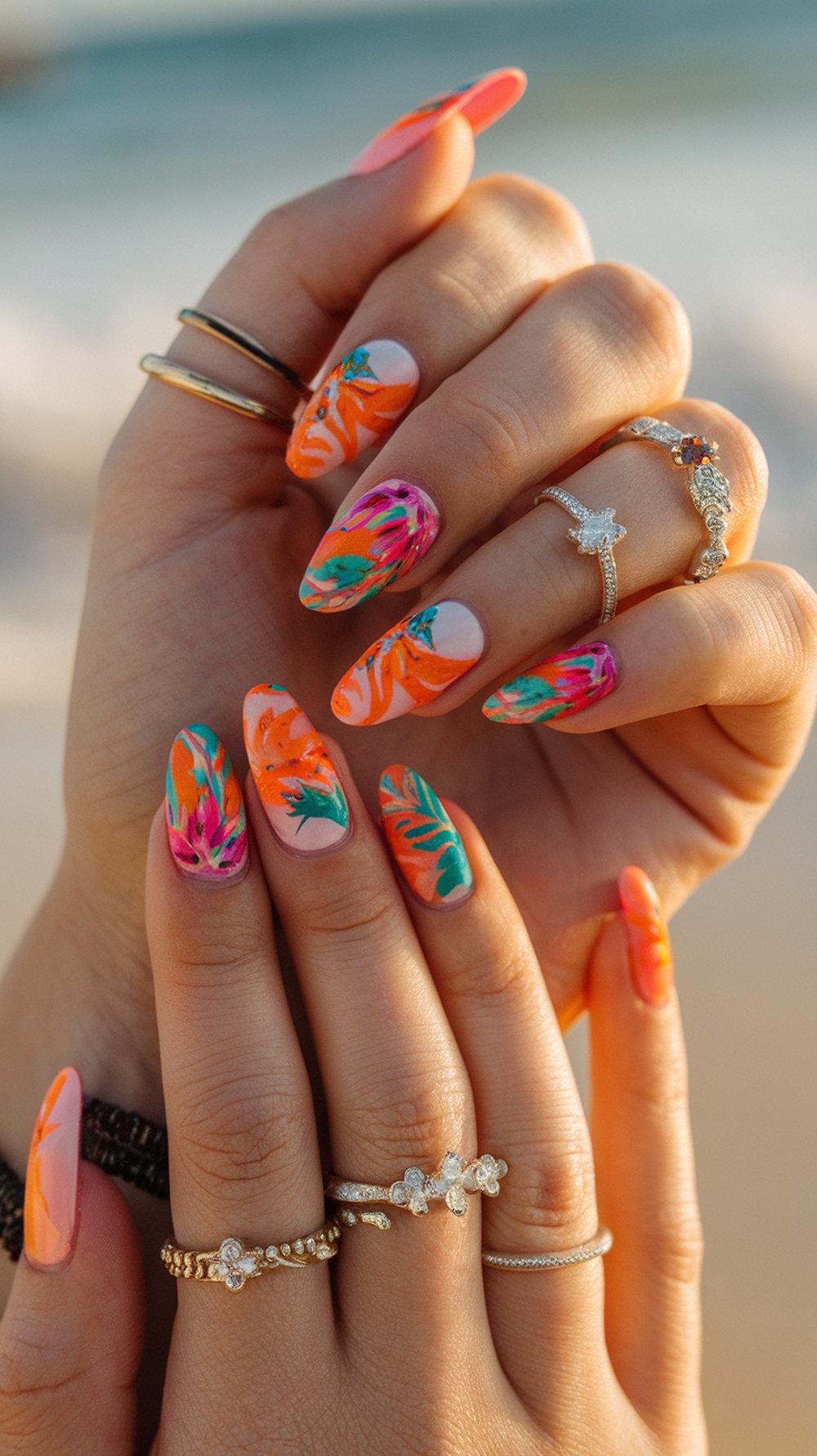 Nails painted in bright tropical colors with floral designs, adorned with rings