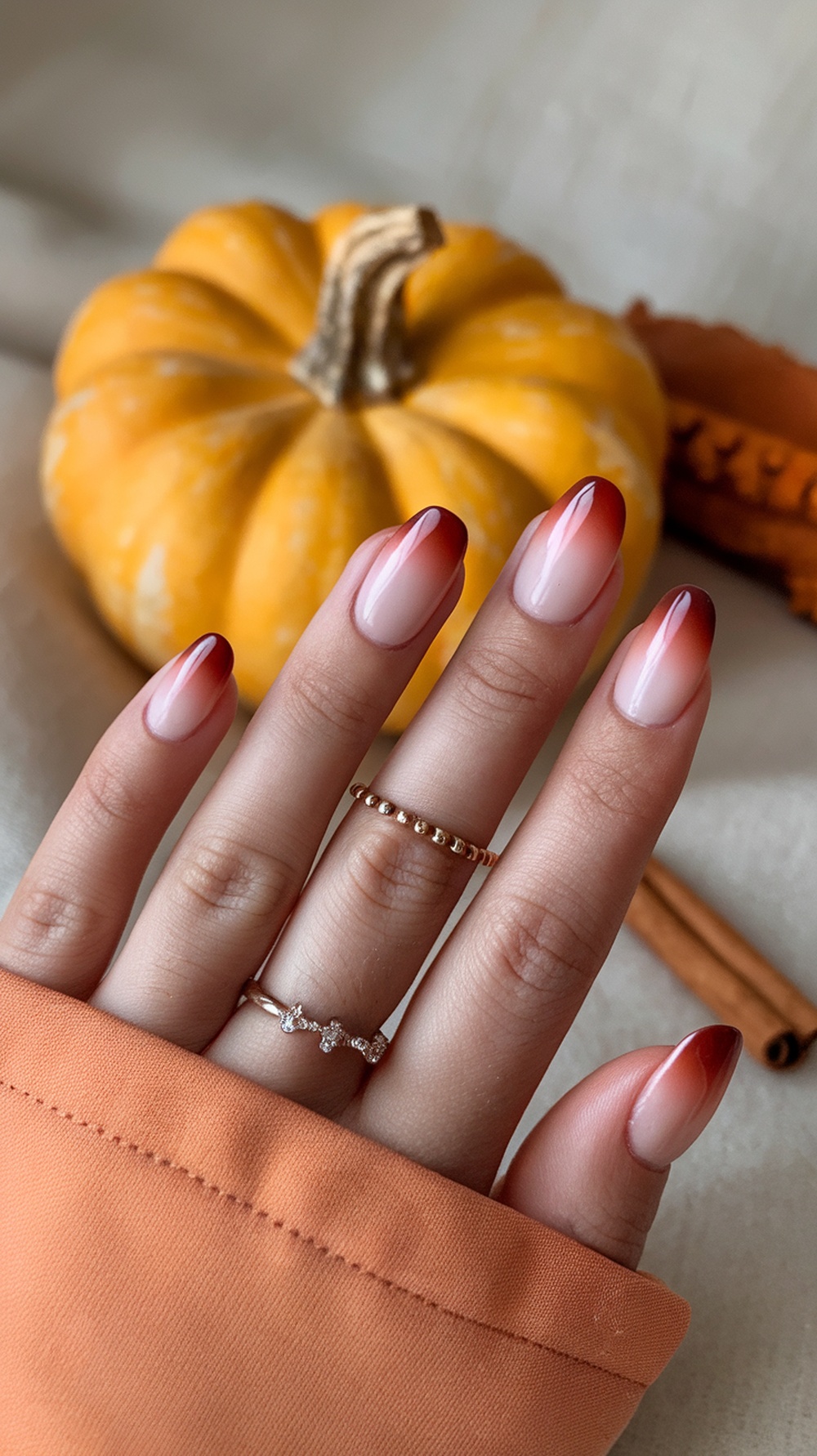 Nails with a pumpkin spice ombré effect, featuring warm tones and a stylish design, placed next to a pumpkin and cinnamon sticks.