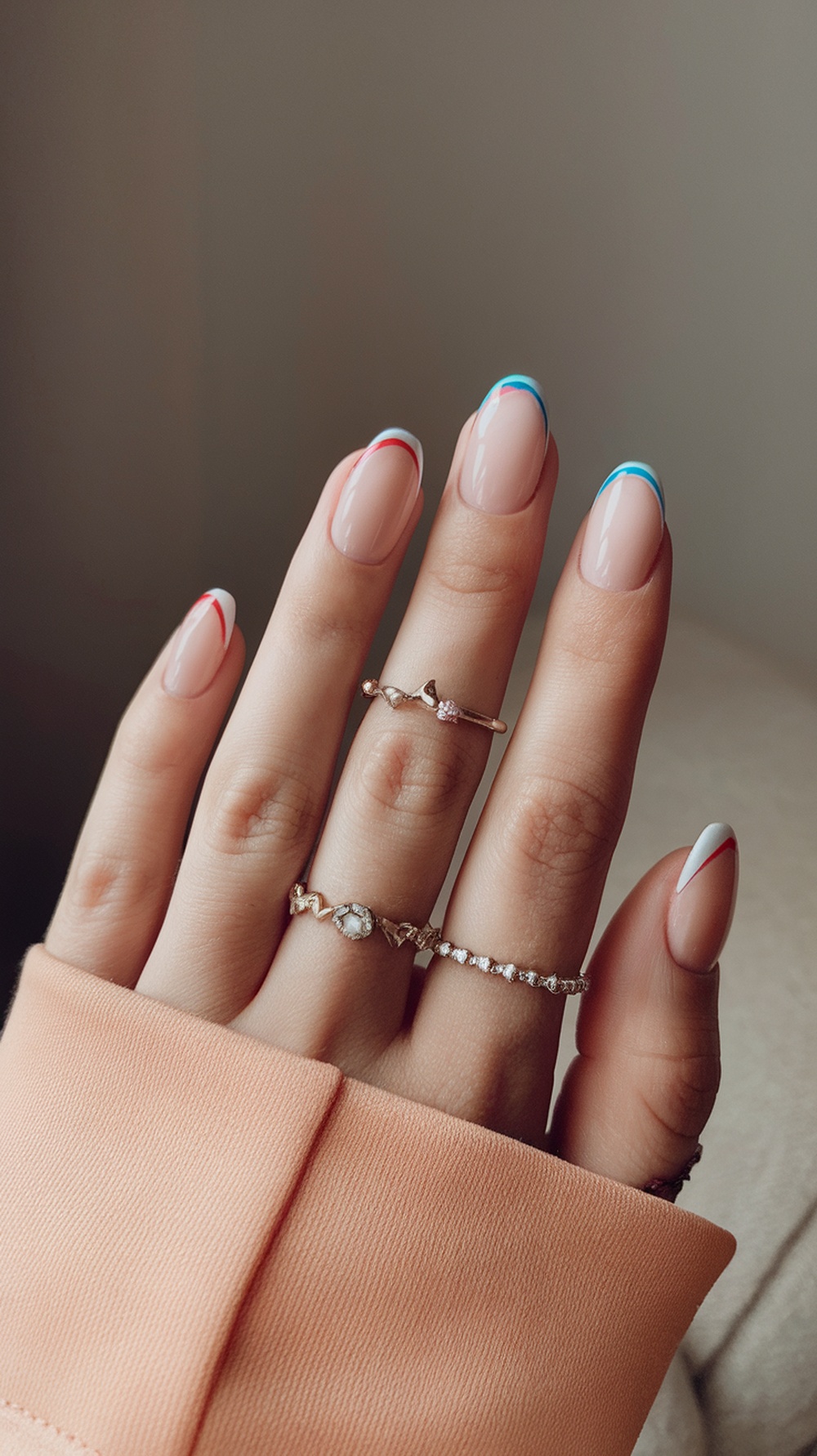 Nails with classic French tips featuring colorful blue and red accents, adorned with delicate rings.