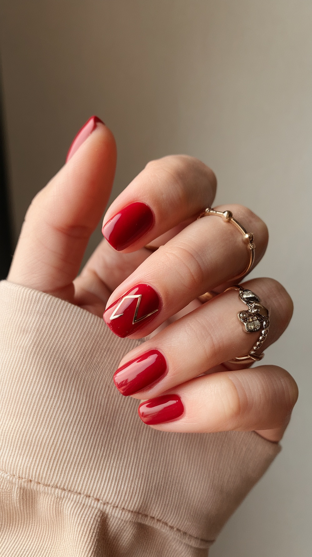 A hand showing a classic red manicure with a zigzag gold accent on one nail.