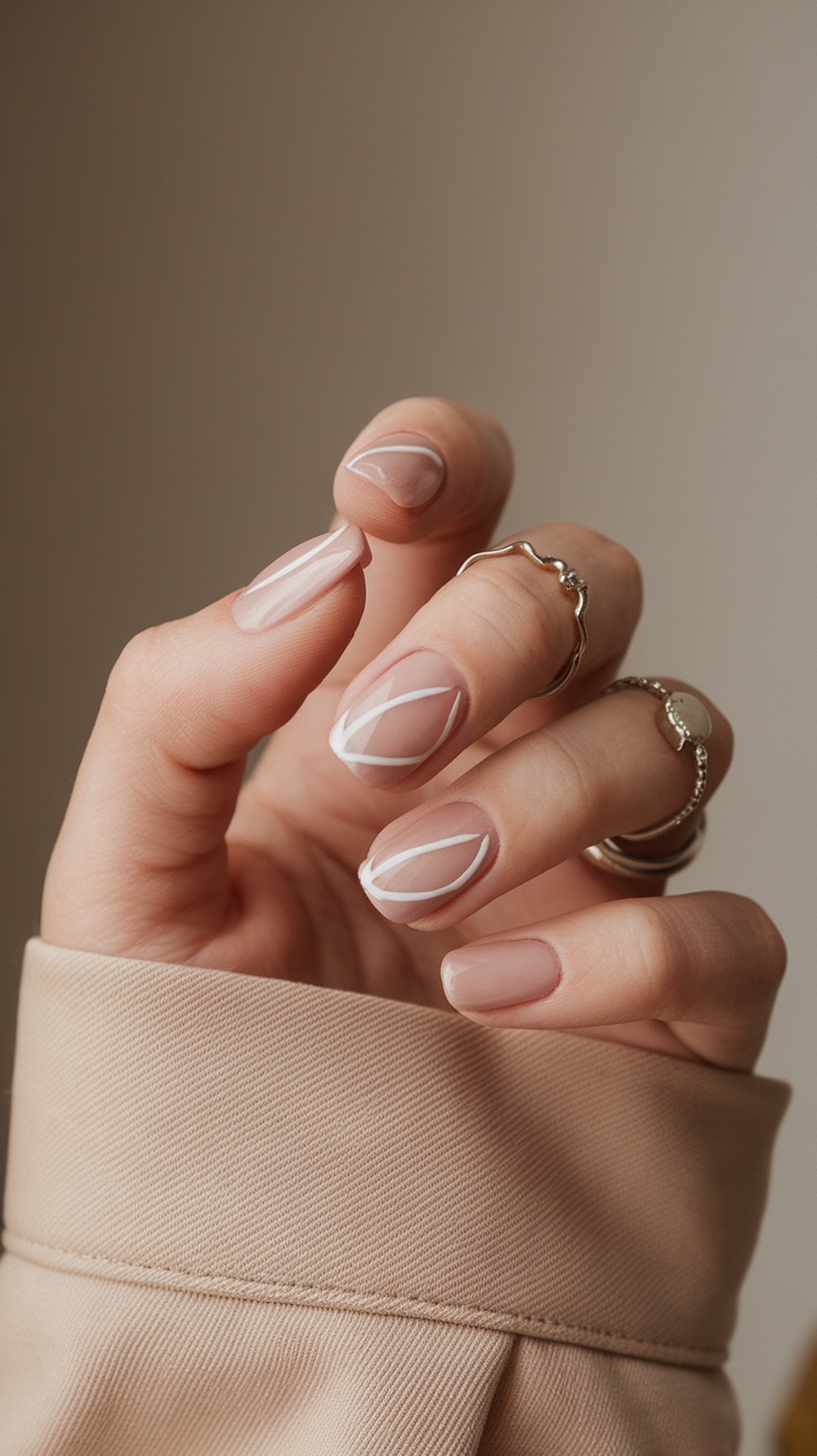 A hand showing color blocked nails with a nude base and white geometric designs.