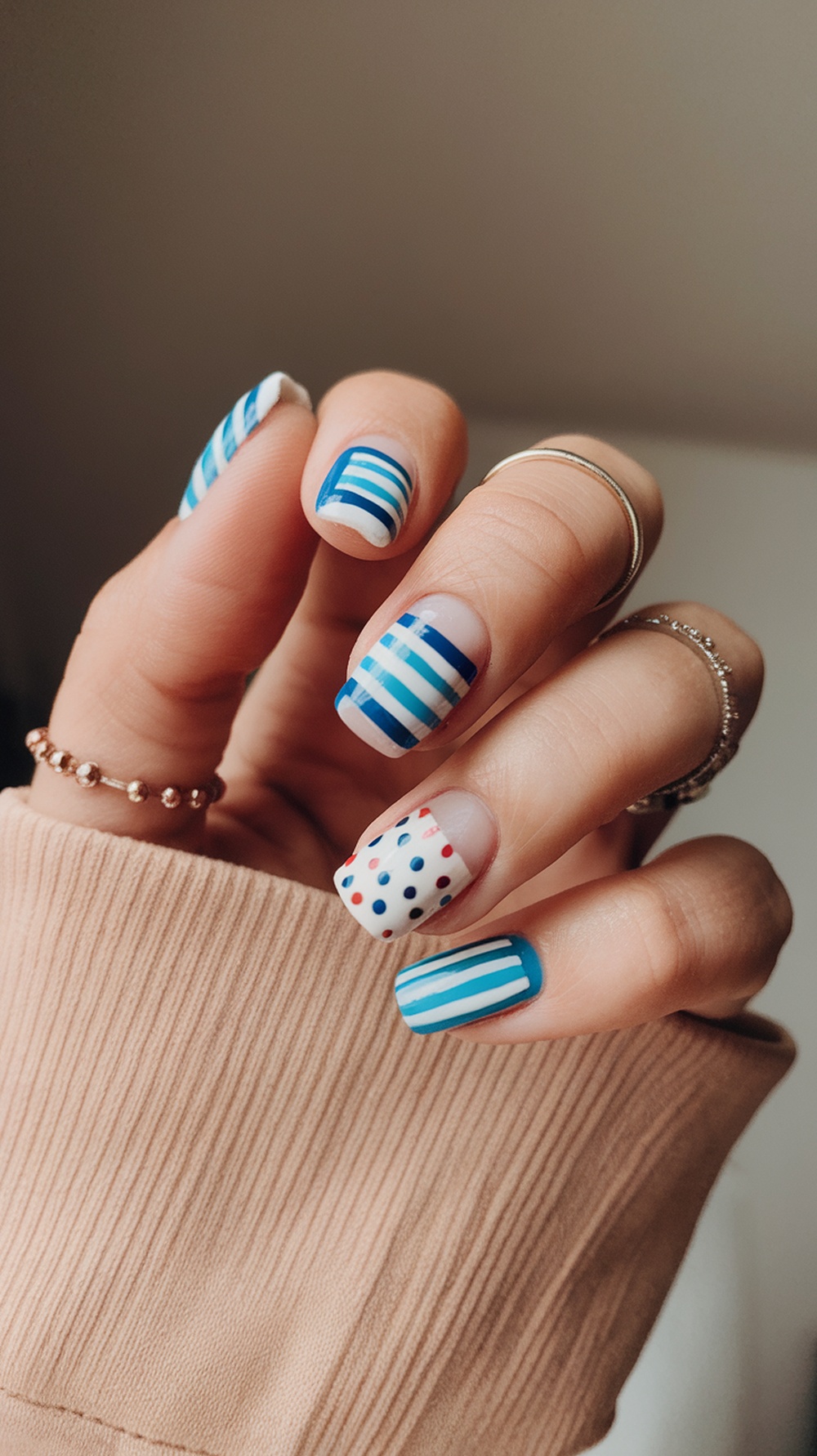 A hand showing short nails with colorful blue stripes and red and white dots.