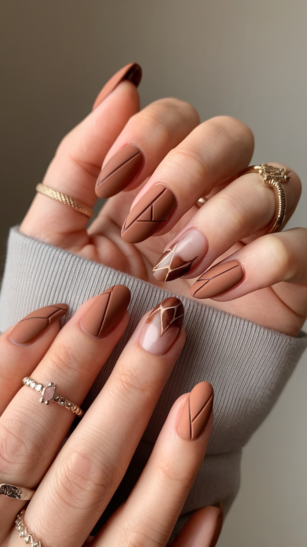 Nails painted in copper brown with geometric designs, featuring a mix of matte and glossy finishes.