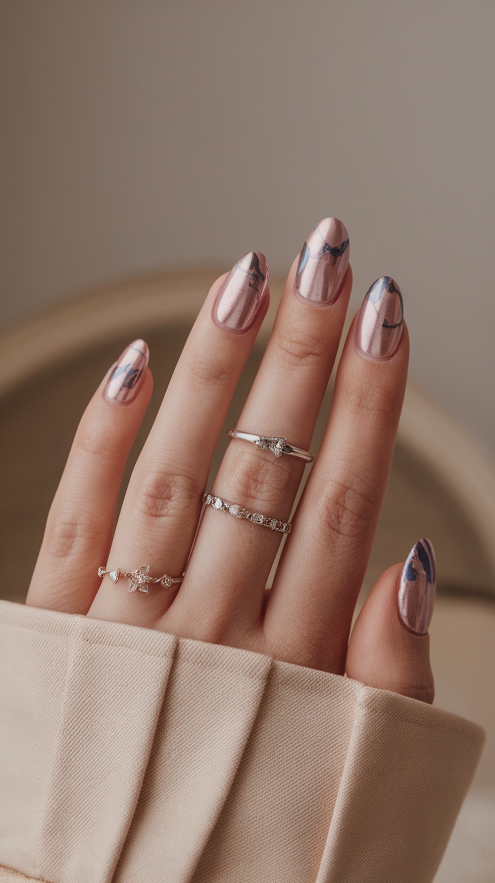 A hand showing cotton candy chrome nails with pink and blue swirls, adorned with silver rings.