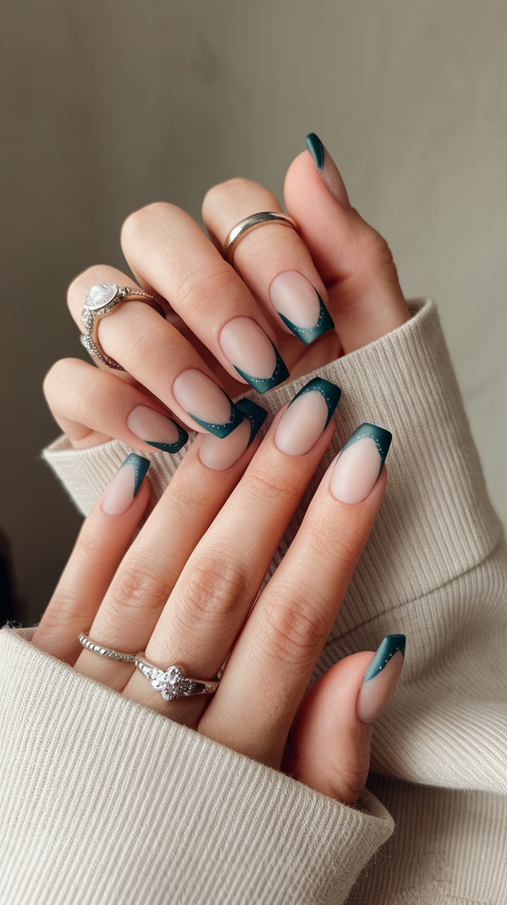 Close-up of hands with dark teal French tip nails and rings, featuring a matte finish.