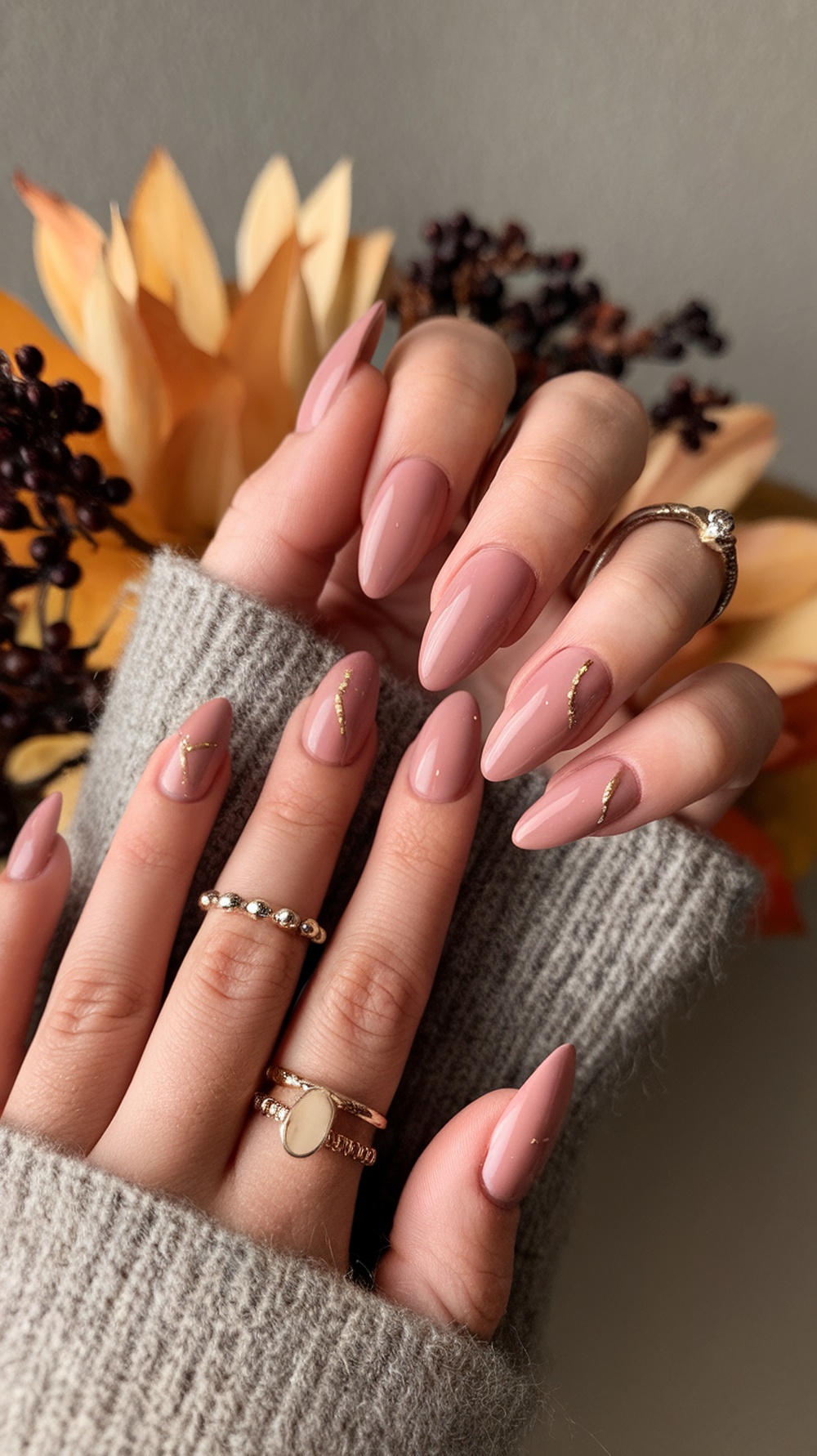 Dusty rose almond nails with gold accents, featuring a cozy sweater and autumn decor in the background.