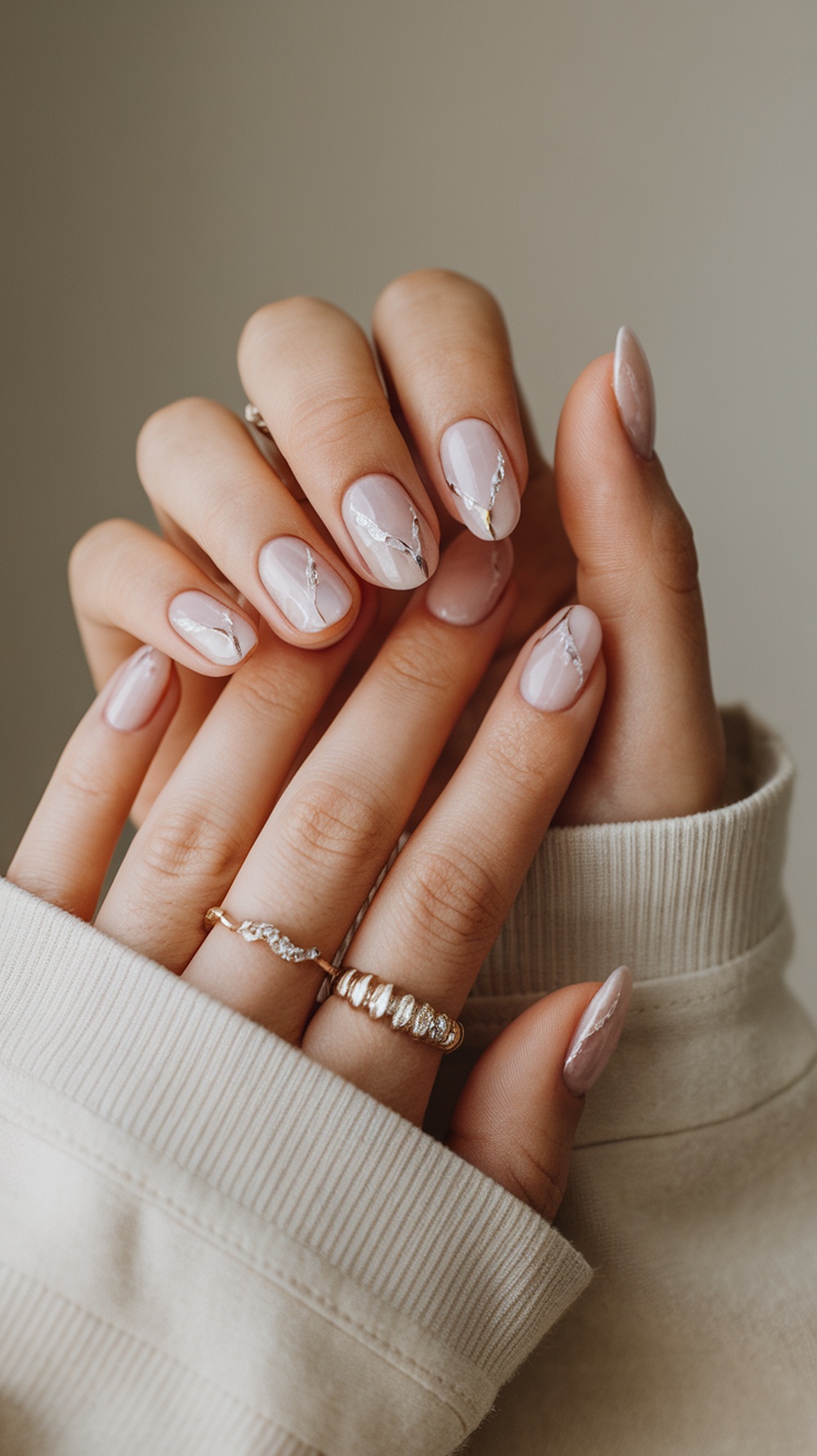 Close-up of elegant ombre soft pink nails with delicate designs and rings.