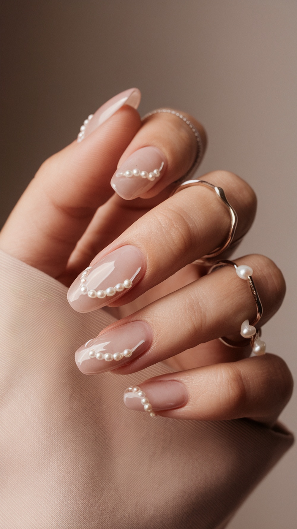 A close-up of elegantly designed nails with pearl accents on a nude base.
