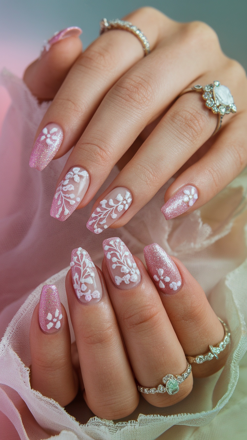 Close-up of hands with pink glitter nails featuring white floral designs.