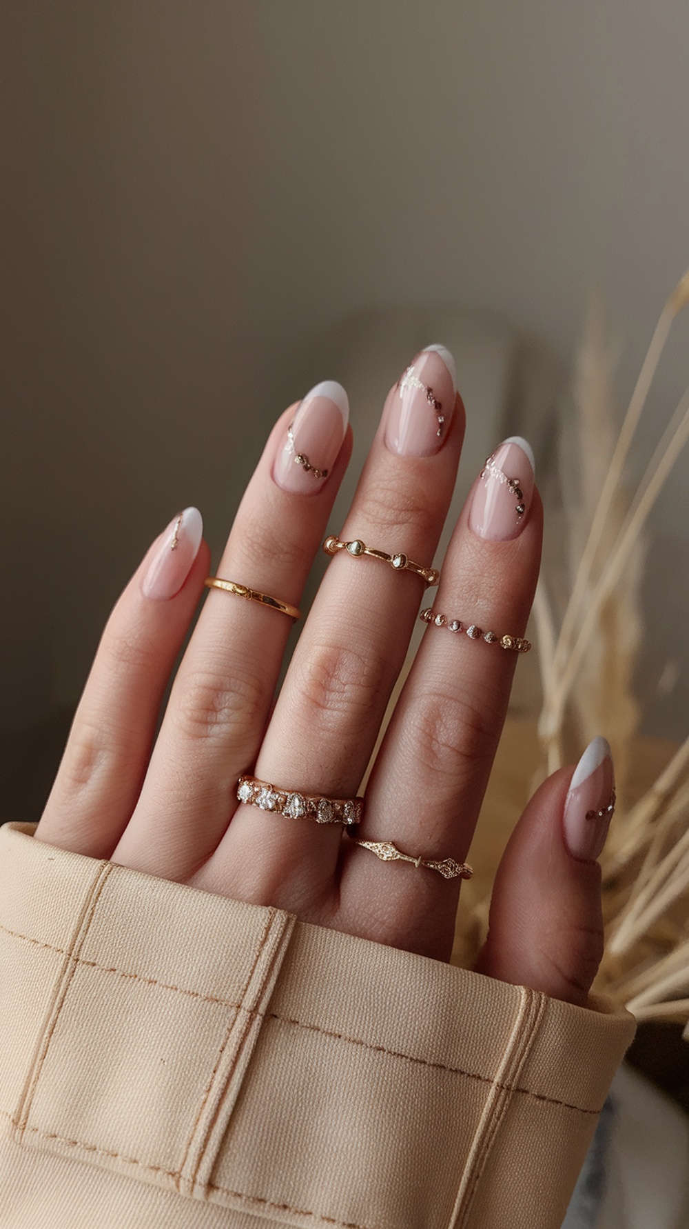Nails with floral accents on a neutral base, featuring a French tip design and gold rings