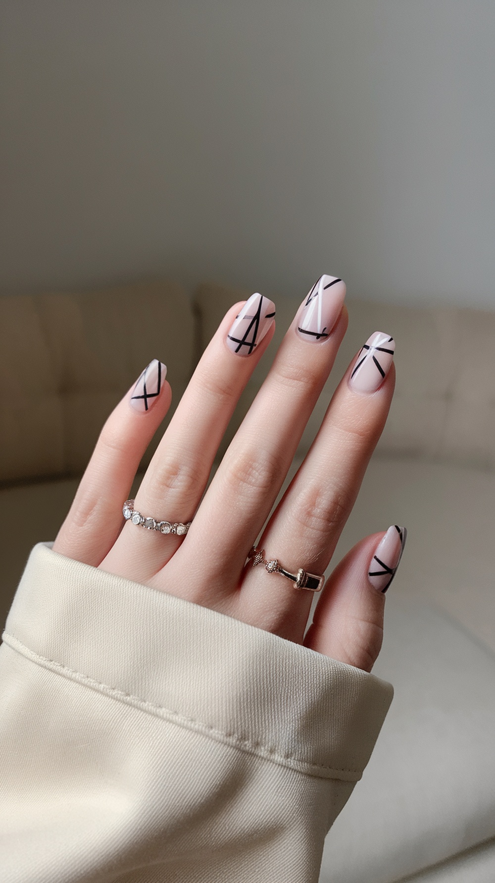 A hand with geometric nail design featuring black lines on a pink background.