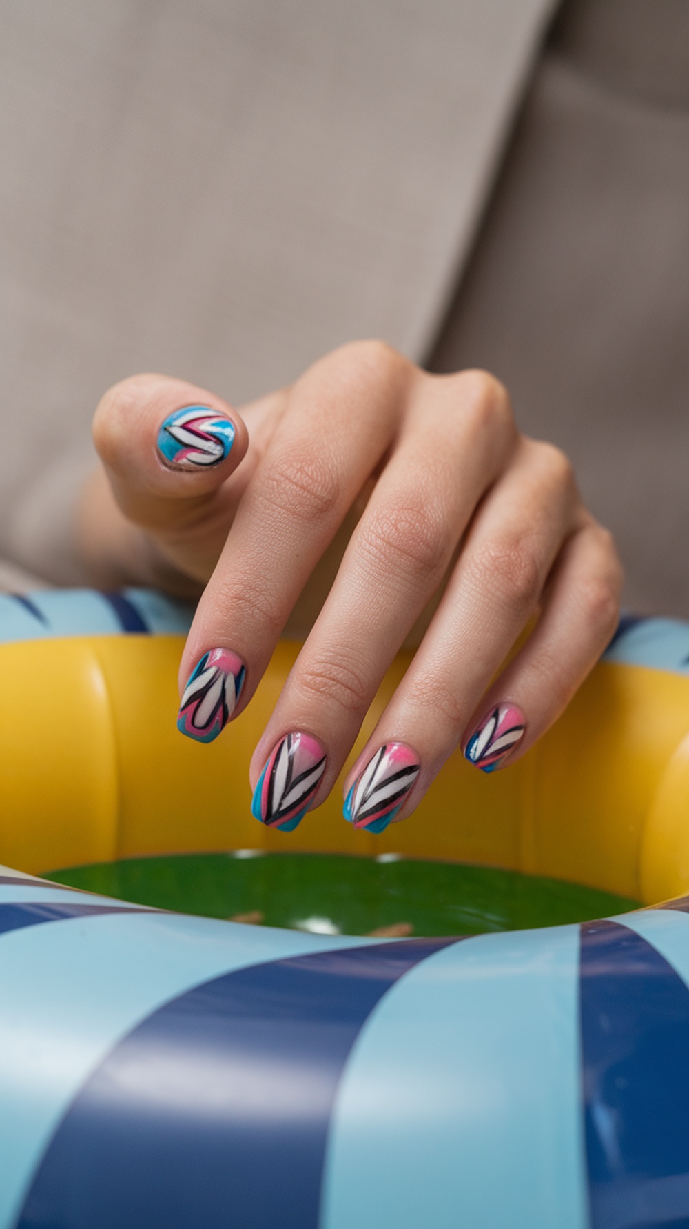 A hand with geometric patterned nails in pink, blue, and black colors, resting on a colorful inflatable ring.