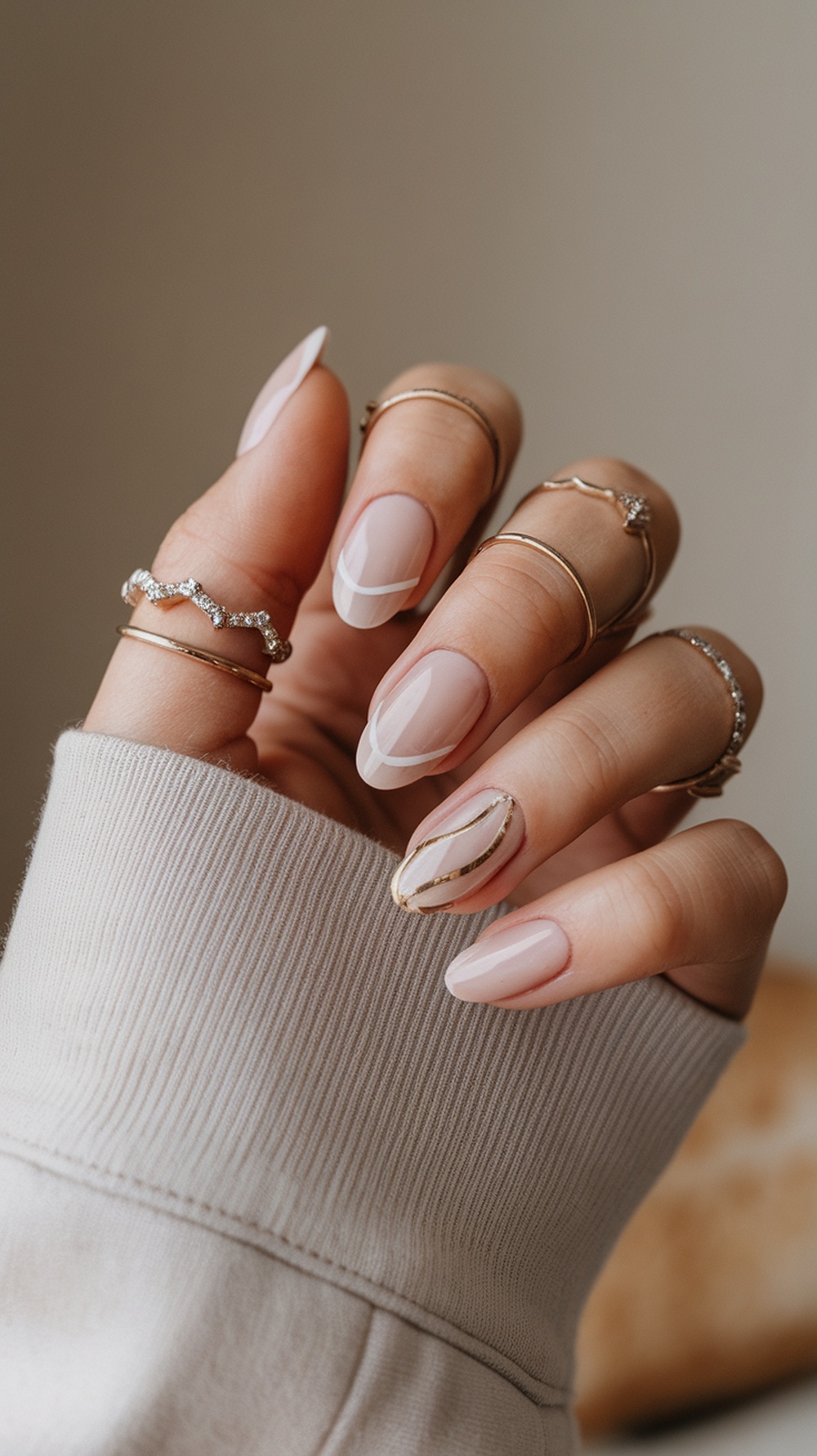 Close-up of square nails with geometric patterns in nude, white, and gold colors.