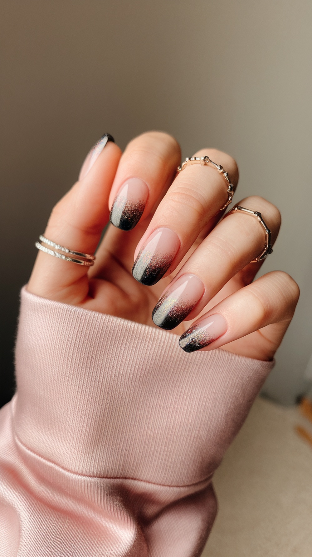 Nails with a glitter ombre effect transitioning from nude to black with sparkles