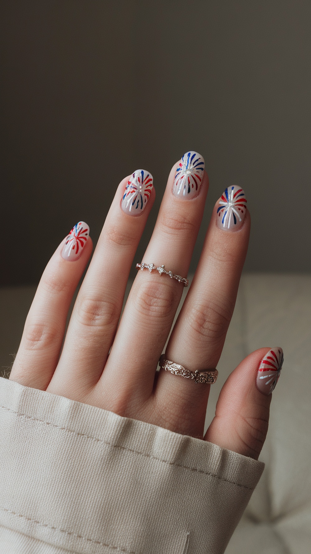 Nail art featuring fireworks design in red and blue on a light background, with rings on fingers.
