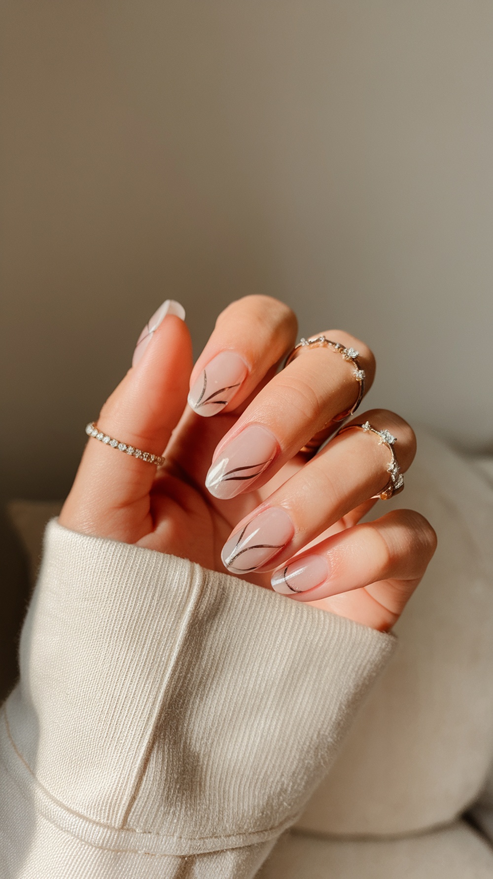 A close-up of a hand with slim, beautifully manicured nails featuring a delicate design, wearing rings and a cozy sweater.