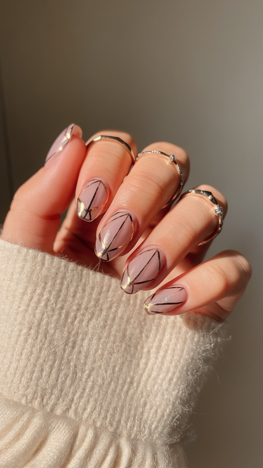 Nails with metallic accents featuring a pink base and gold and black geometric designs.
