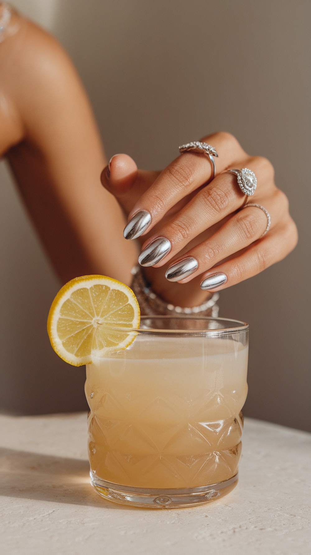 A close-up of metallic silver nails next to a cocktail with a lemon slice.