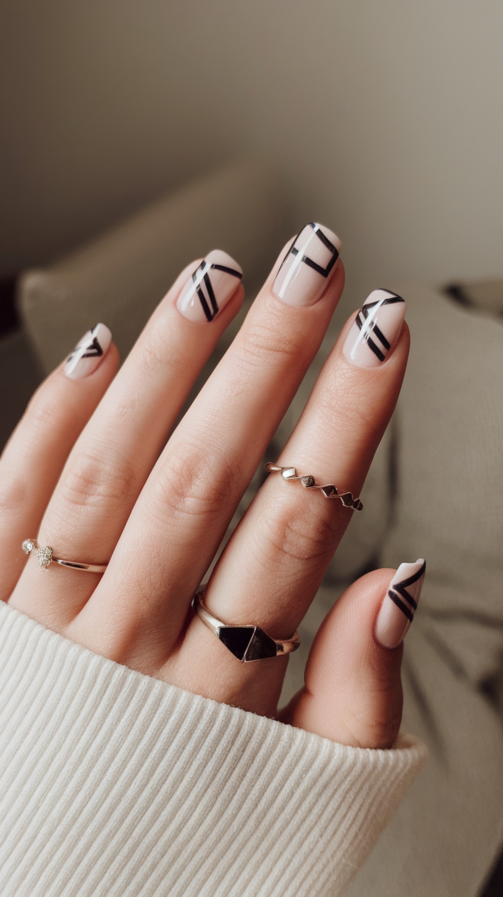 Close-up of short nails with minimalist geometric patterns in black on a nude base