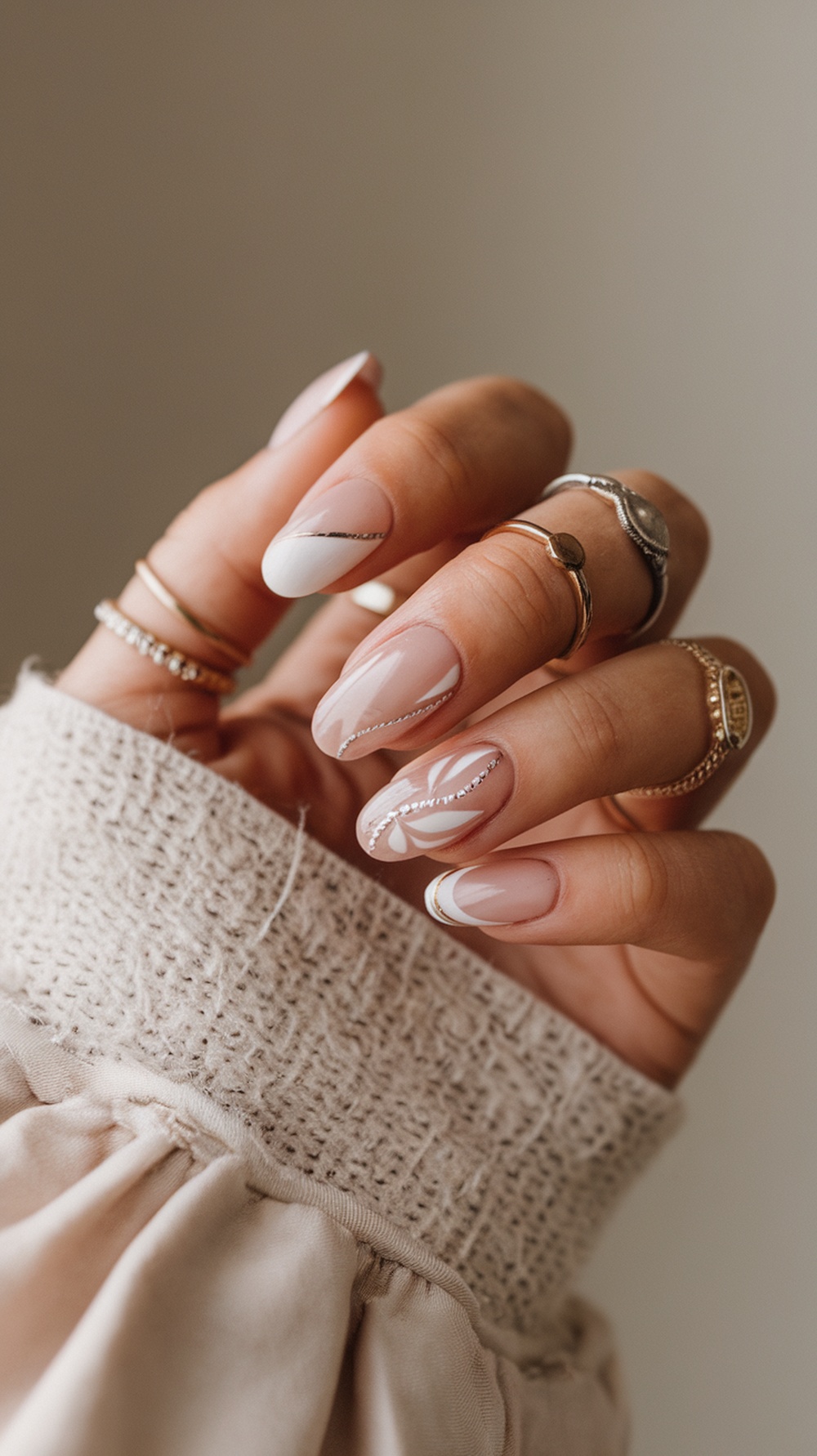 A close-up of a hand with minimalist summer chic nails, featuring soft neutral tones and delicate designs, adorned with simple rings.