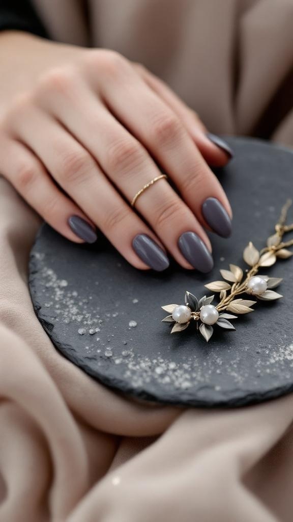 A close-up image of hands with muted gray almond nails, featuring delicate white lines and gold rings on the fingers.